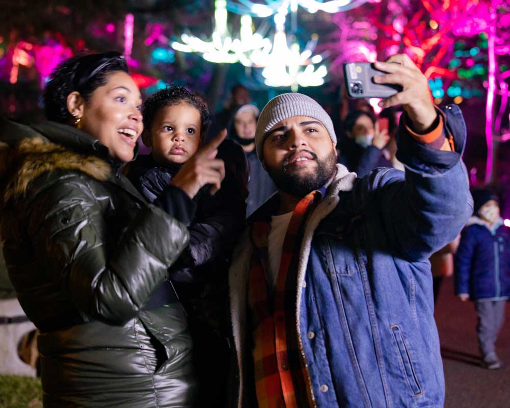 A family poses in front of illuminated trees.